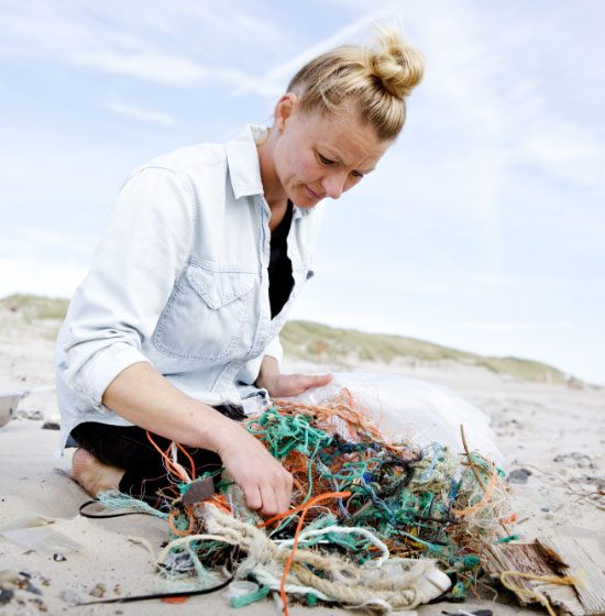 Frau sammelt verschiedene Abfälle an einem Strand